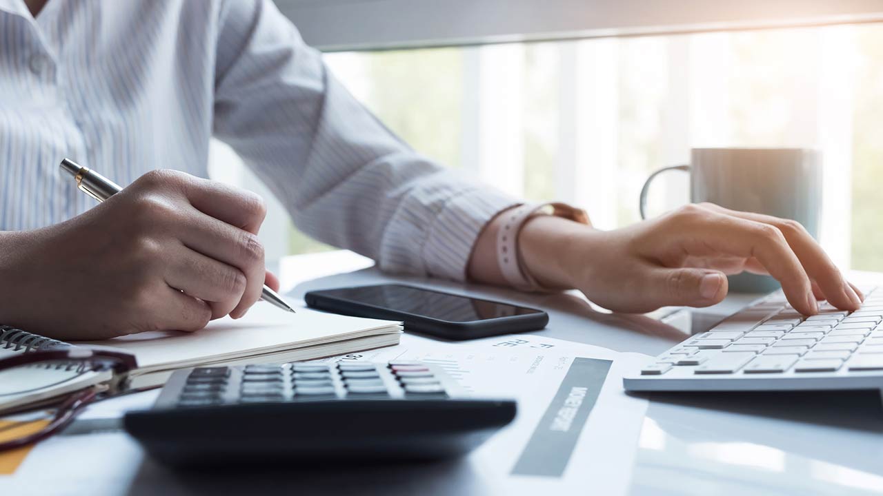 Woman using computer and calculator during note some data on notepad for calculate financial at home office