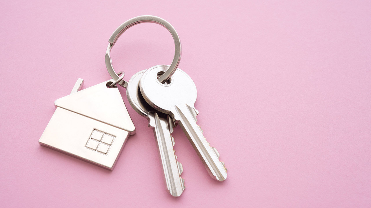 Silver house key with house keychain on pink background