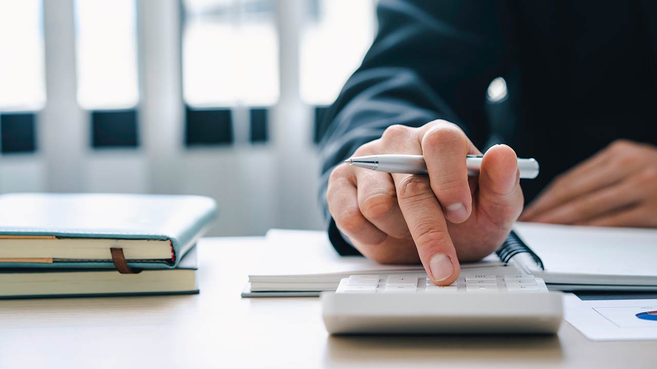 Businessman presses a calculator on a desk with notebooks