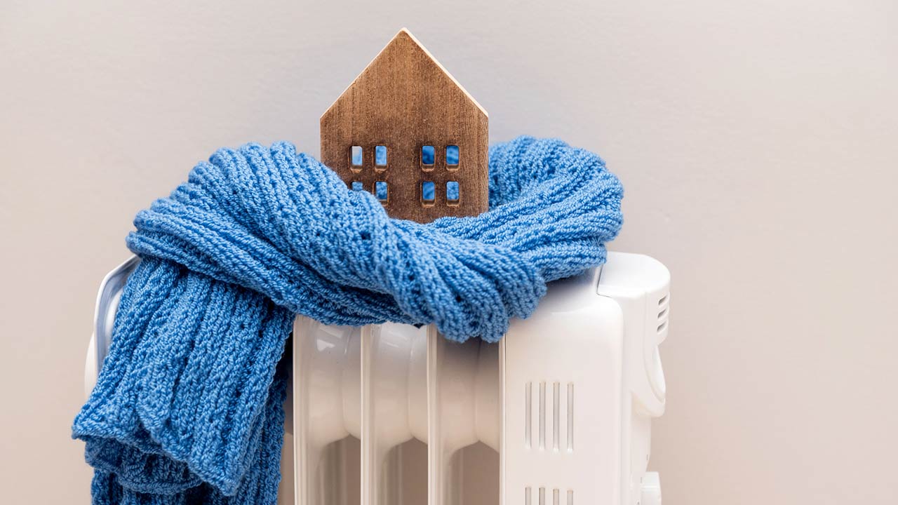 Wooden model house wrapped in a blue scarf on a radiator