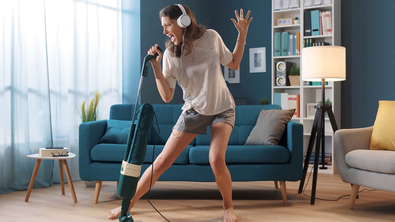 Cheerful woman cleaning up her home and singing, using the vacuum cleaner as a microphone