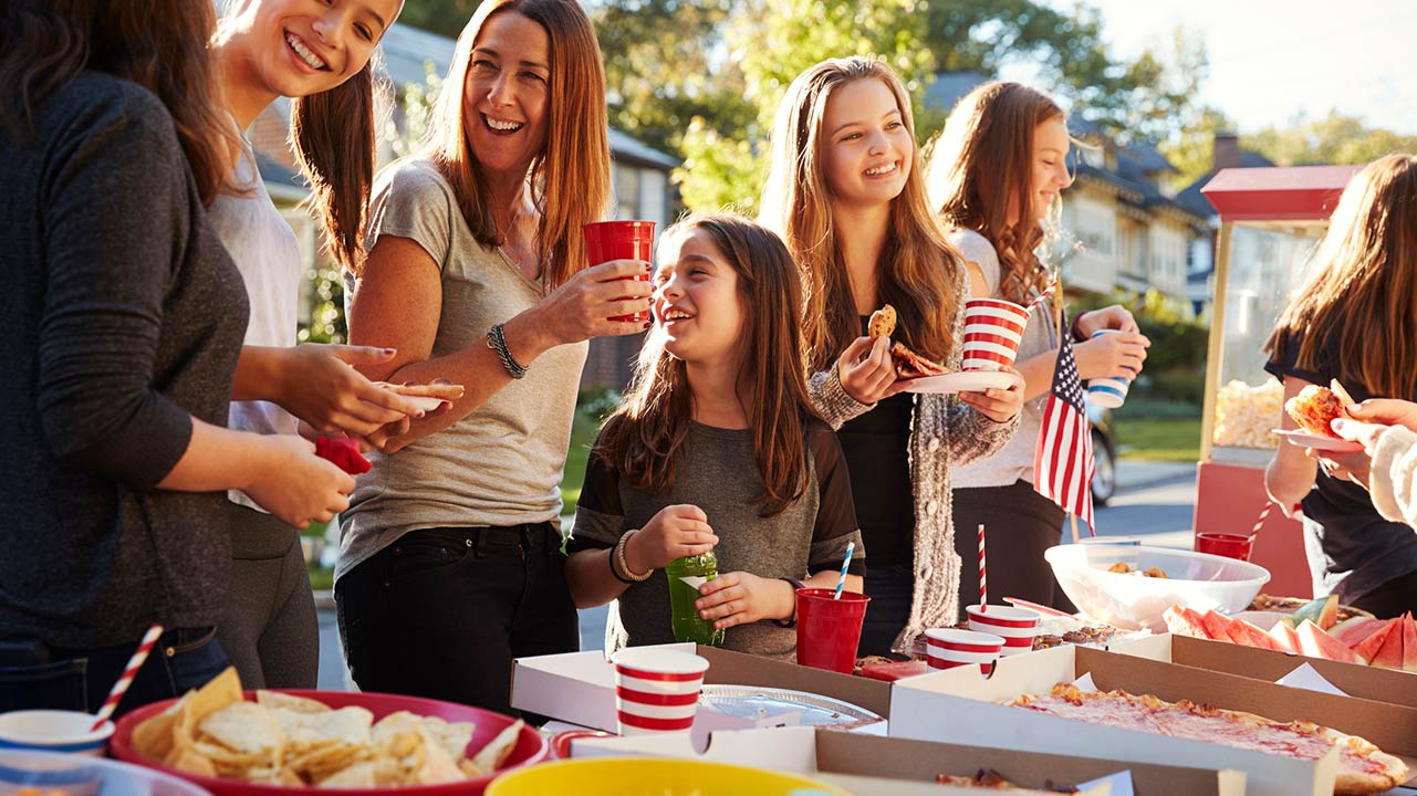 Girls stand talking at a block party food table, close up