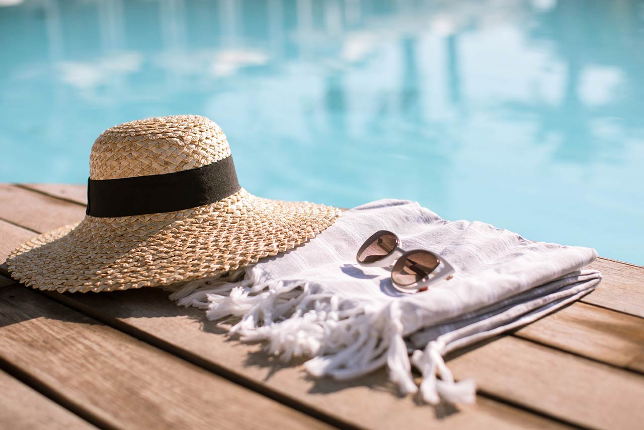 Sunglasses and straw hat on the wooden floor at the pool