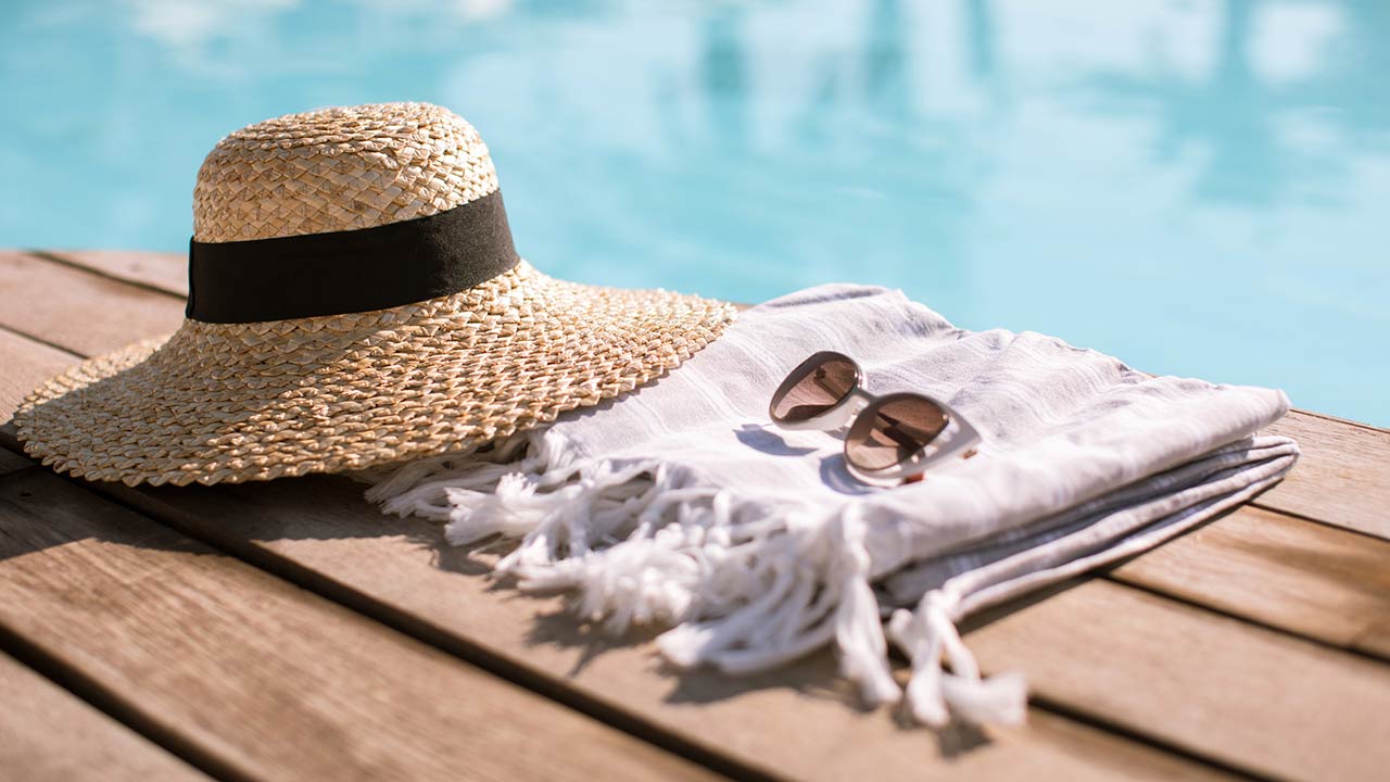 Sunglasses and straw hat on the wooden floor at the pool